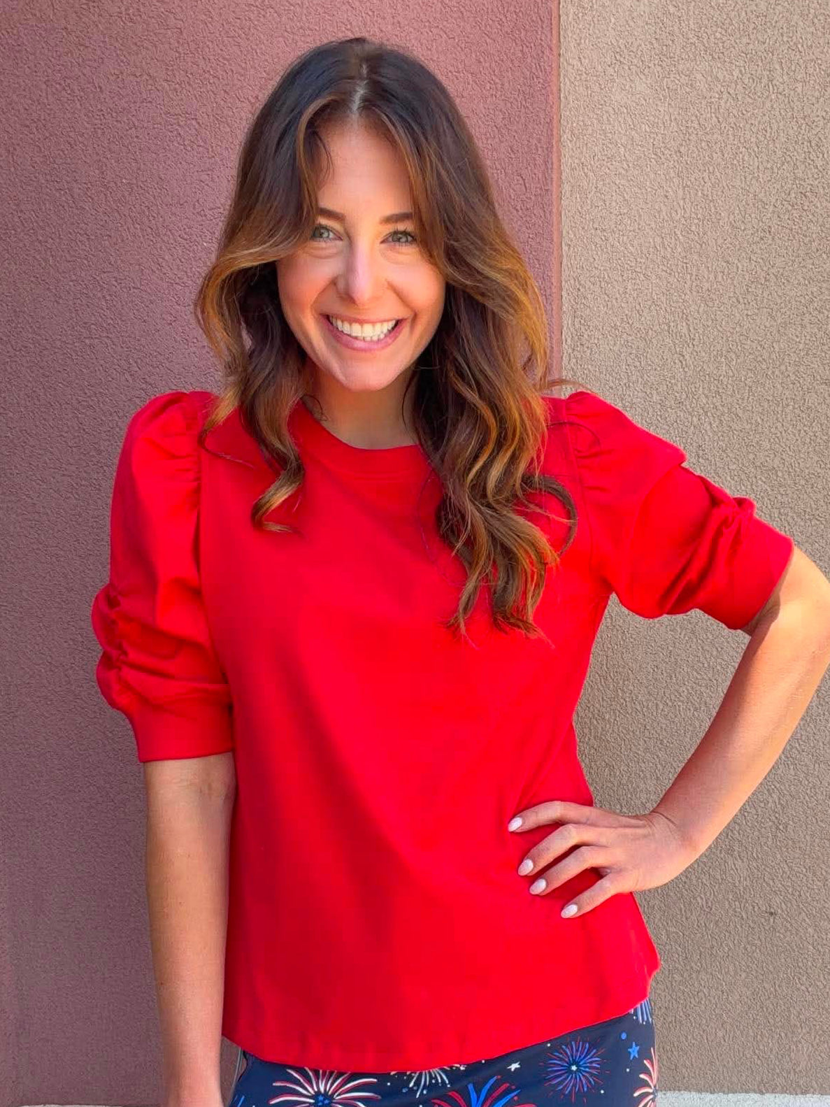 Woman wearing a red top and a blue skirt with firework patterns against a plain background